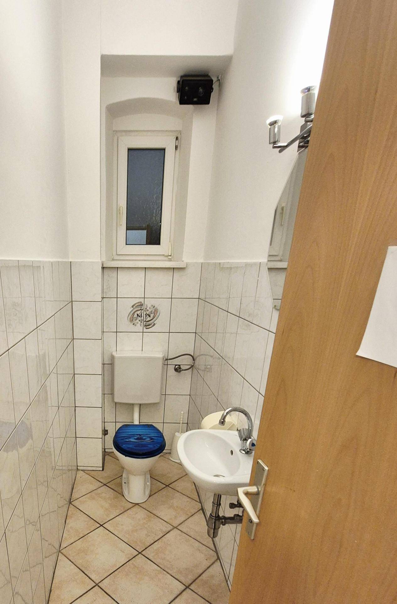 Kleines Gäste-WC mit Toilette, Waschbecken und Fenster, ausgestattet mit hellen Fliesen.