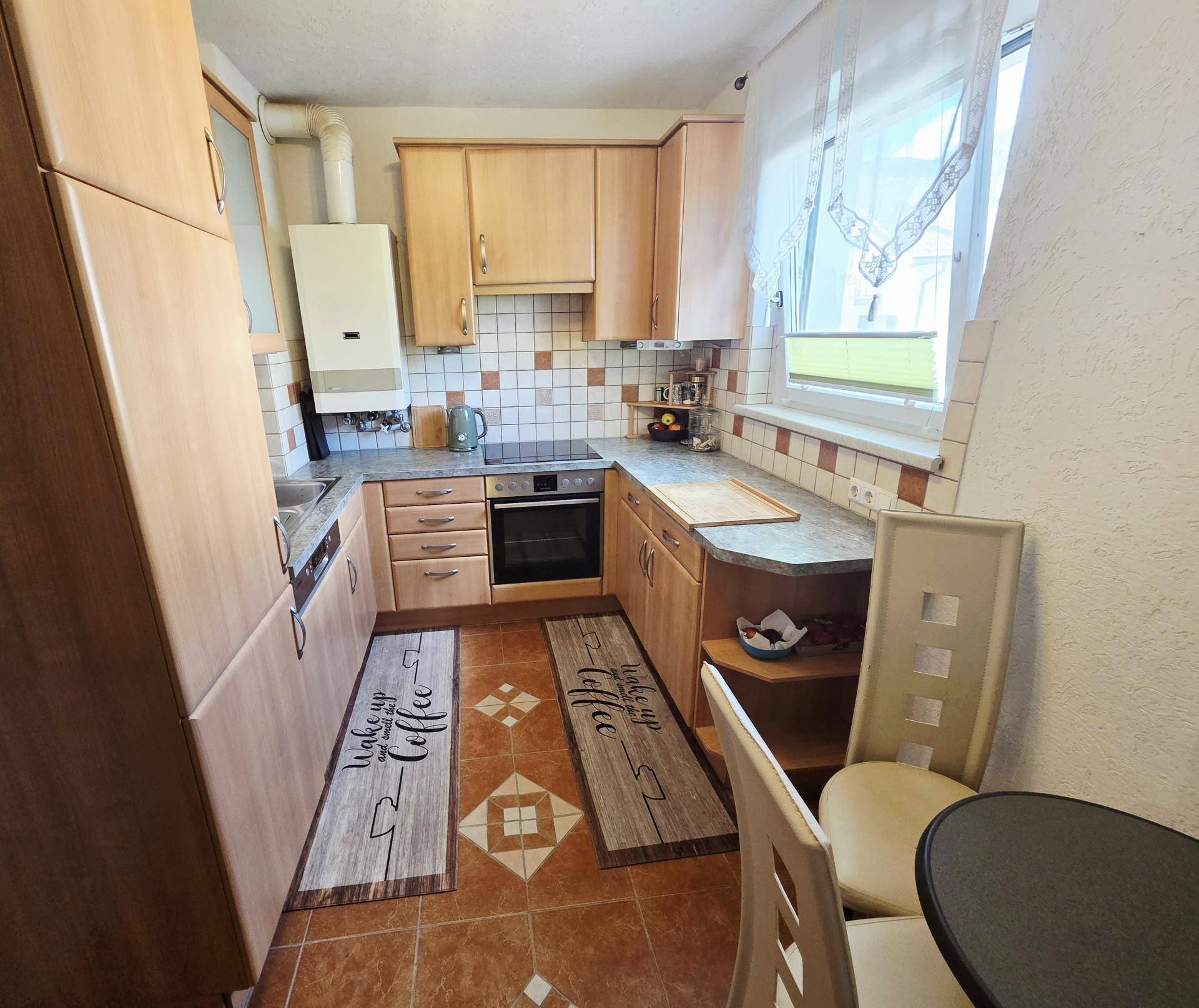 Funktionale Küche mit Holzschränken, integrierten Geräten und einem Gasboiler an der Wand.