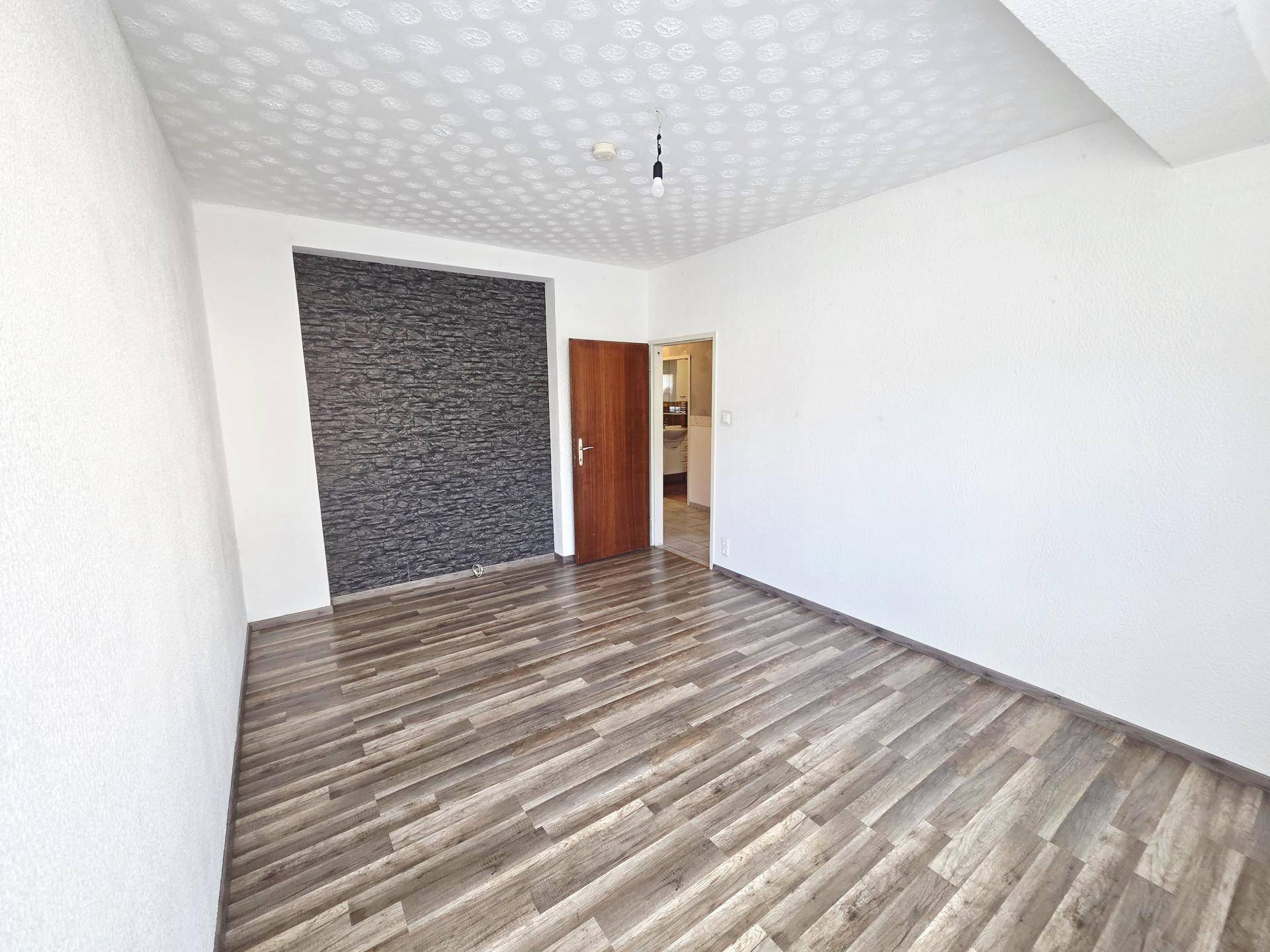 Geräumiges, leeres Zimmer mit Laminatboden und einer Akzentwand in dunkler Steinoptik.