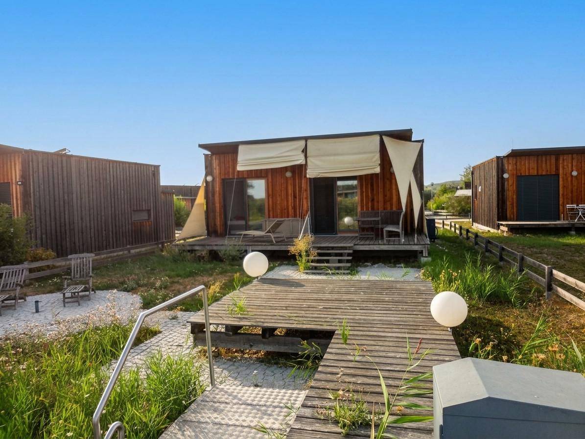 Mehrere moderne Holzhäuser mit Terrassen und Sitzgelegenheiten in naturnaher Umgebung.