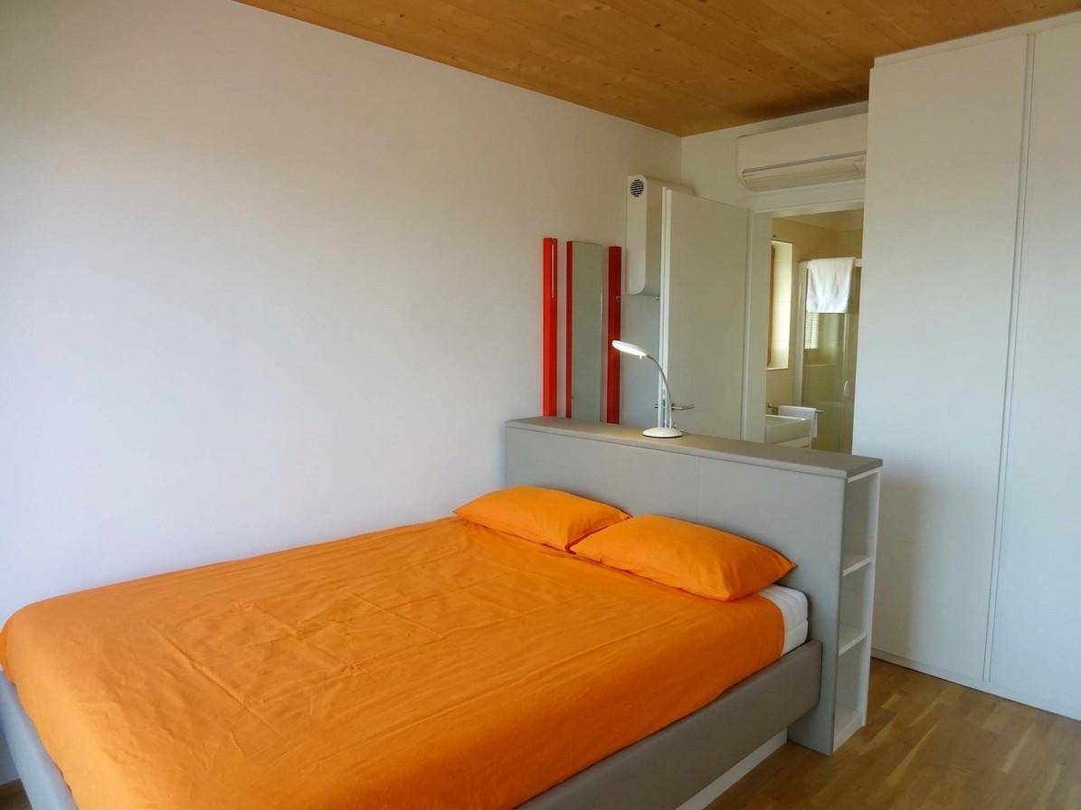 Schlafzimmer mit Doppelbett, orangefarbener Bettwäsche, Einbauschrank und Klimaanlage.