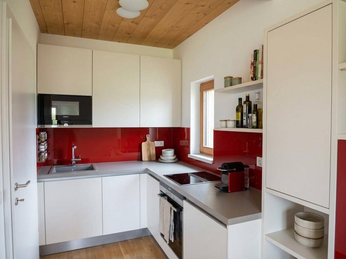 Moderne Küche mit weißen Schränken, roter Rückwand, Induktionskochfeld und Fenster.