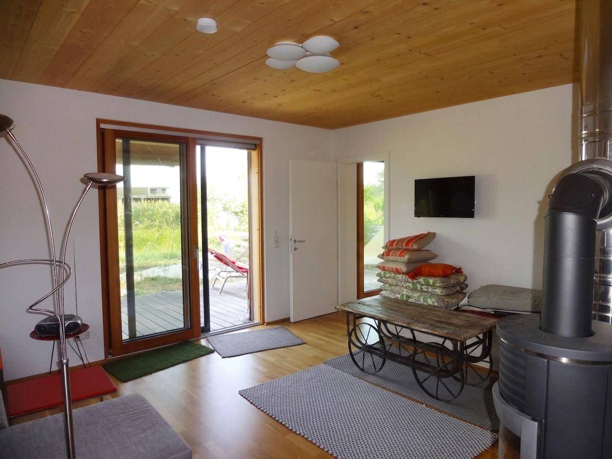 Gemütliches Wohnzimmer mit Kaminofen, Holzboden und Zugang zur Terrasse durch Schiebetür.