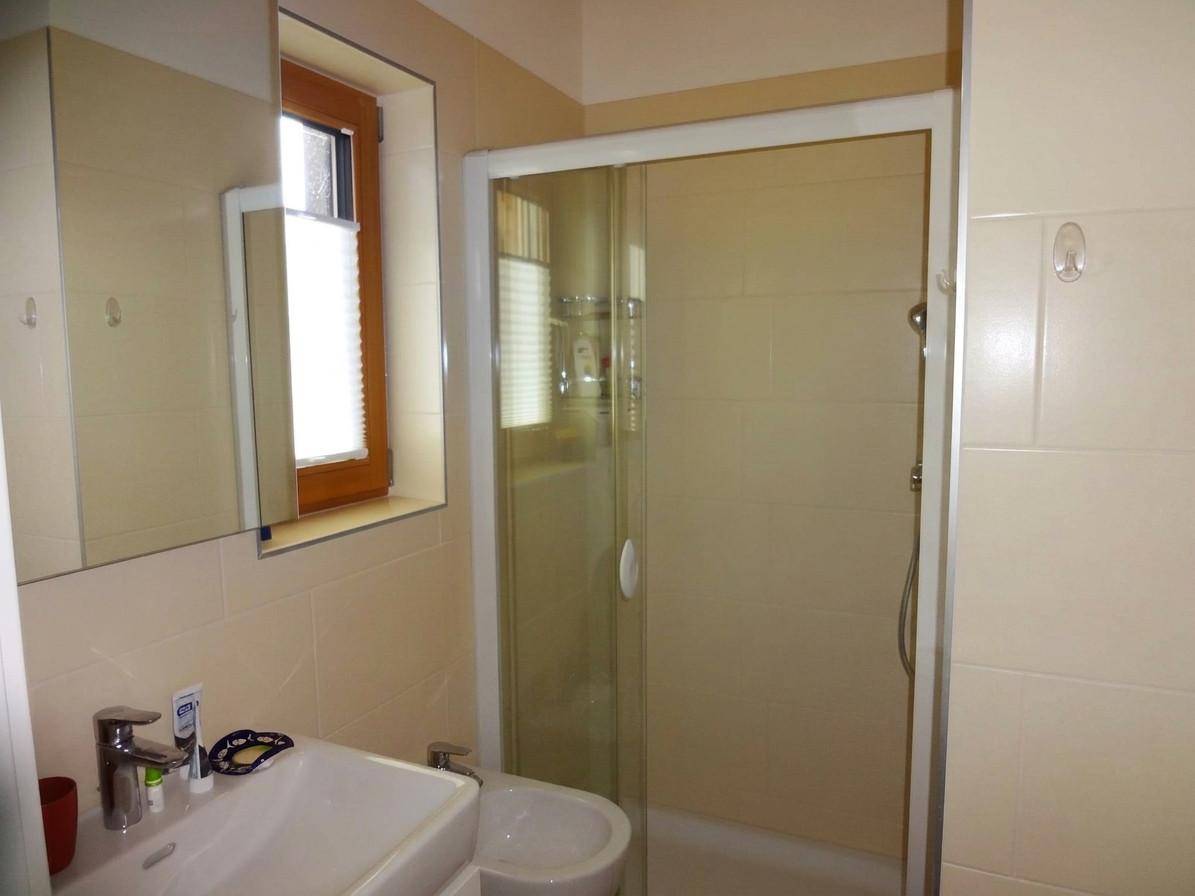 Badezimmer mit Duschkabine, Waschbecken, Bidet und Fenster in hellen Beigetönen.