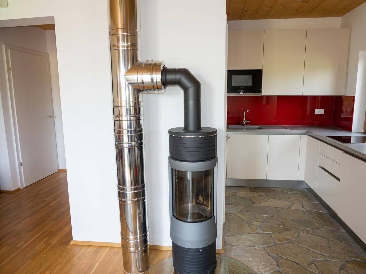 Moderner Kaminofen im Übergangsbereich zur Küche mit roter Rückwand und Steinboden.