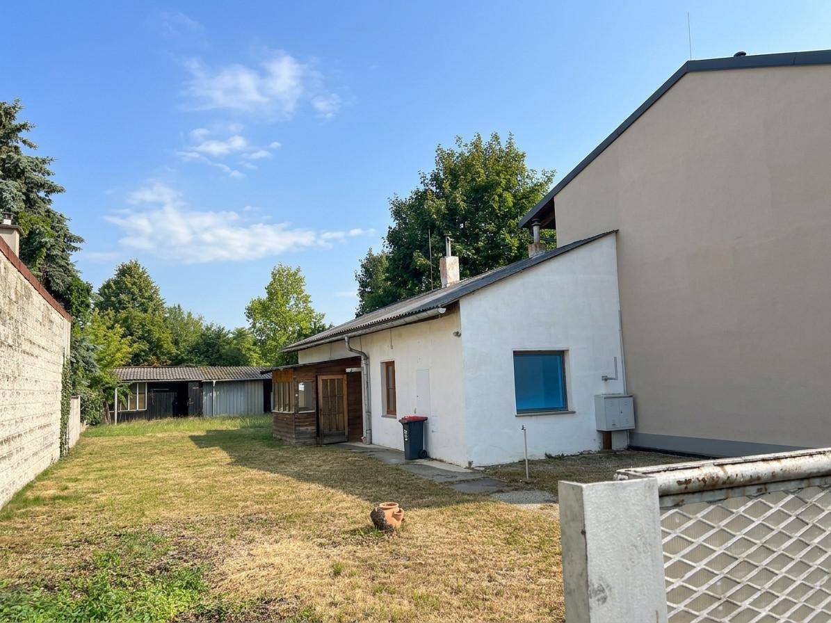 Außenansicht eines kleinen weißen Hauses mit blauen Fenstern und einem ungepflegten Gartenbereich.