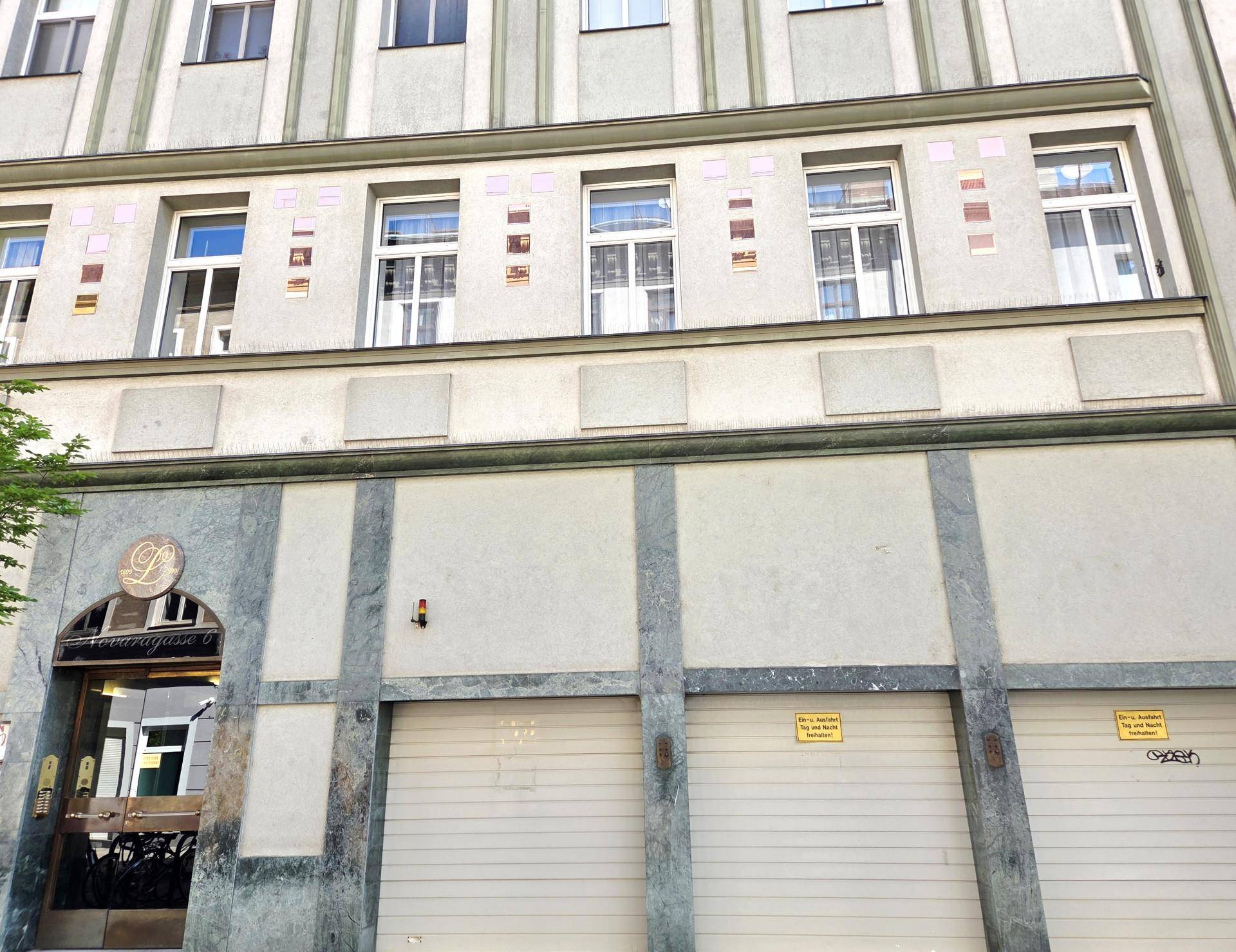 Fassade eines Mehrfamilienhauses mit mehreren Fenstern und geschlossenen Garagentoren im Erdgeschoss.