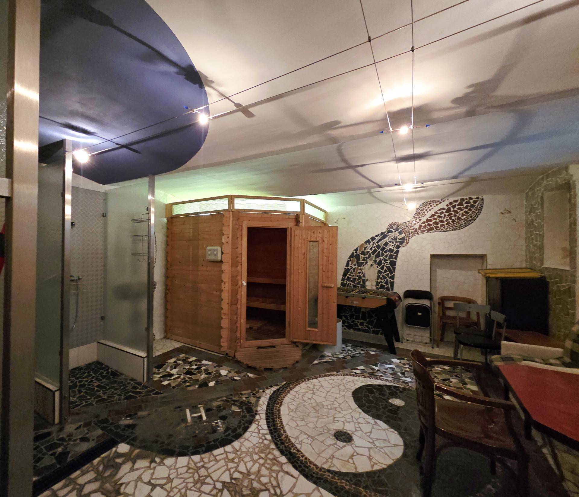 Exklusiver Wellnessbereich mit einer Holzsauna, Dusche und einem einzigartigen Yin-Yang-Mosaik auf dem Boden.