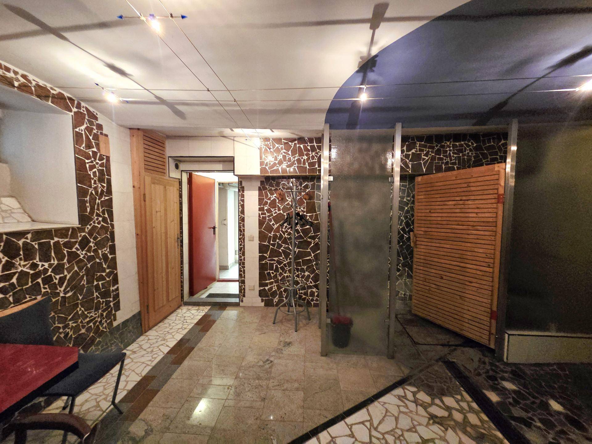 Wellnessbereich mit Dusche, kunstvollen Mosaikfliesen und dem Eingang zu einer Sauna, in einem entspannenden Ambiente.