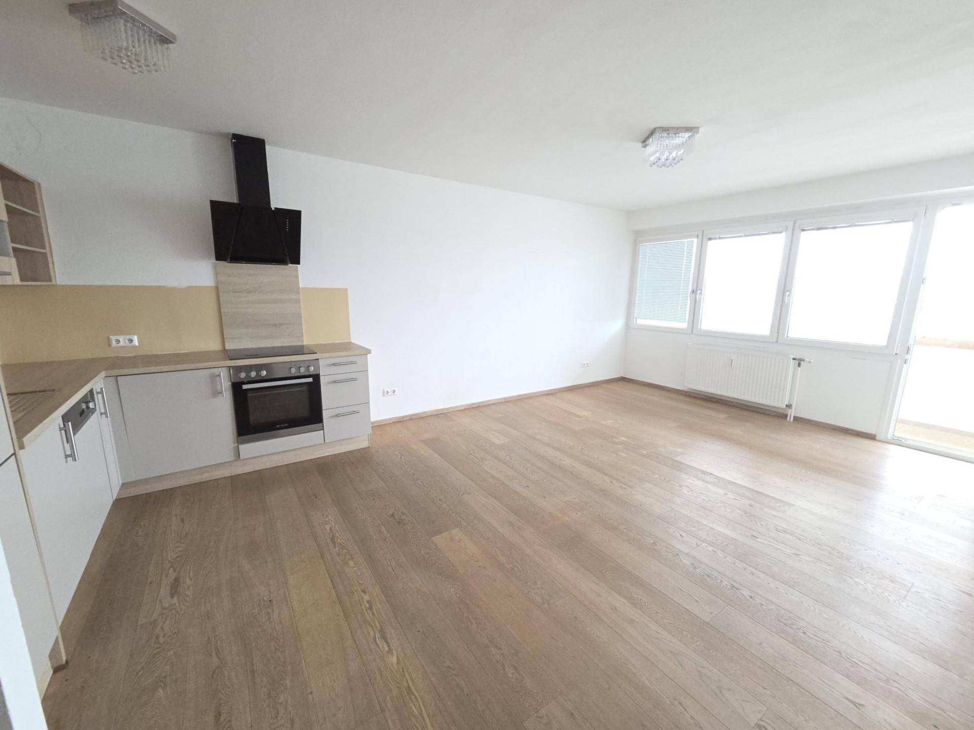Heller offener Wohnbereich mit moderner Einbauküche, elegantem Holzboden und direktem Zugang zum Balkon.