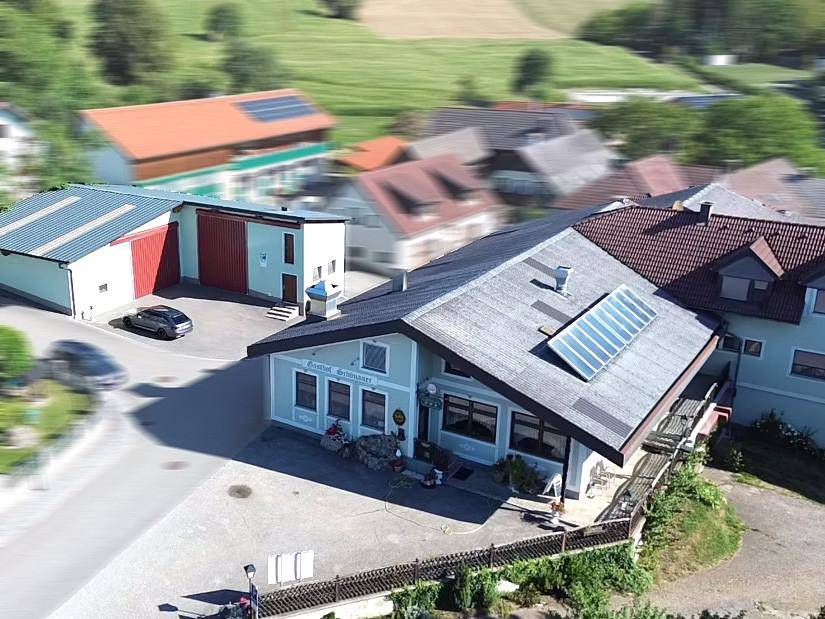 Luftaufnahme des Gasthauses mit Solarpaneelen auf dem Dach und umliegenden Gebäuden in ländlicher Umgebung.