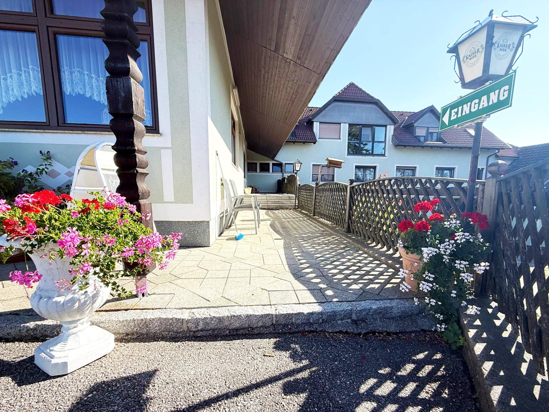Eingangsbereich des Gasthauses mit einer Rampe, umgeben von Blumenkübeln und einem Holzzaun.