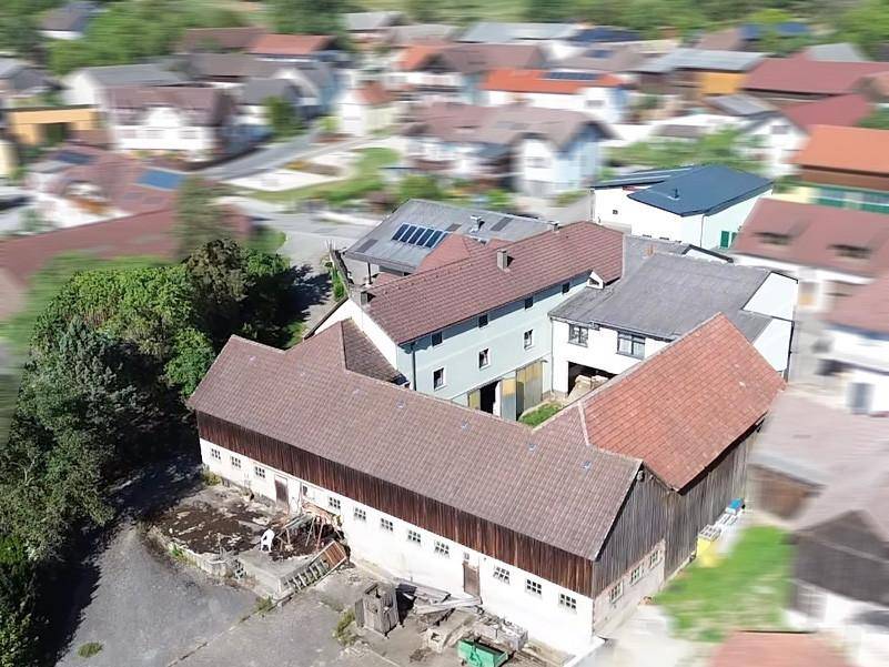 Luftaufnahme eines Gebäudekomplexes mit verschiedenen Dächern und angrenzenden ländlichen Strukturen.