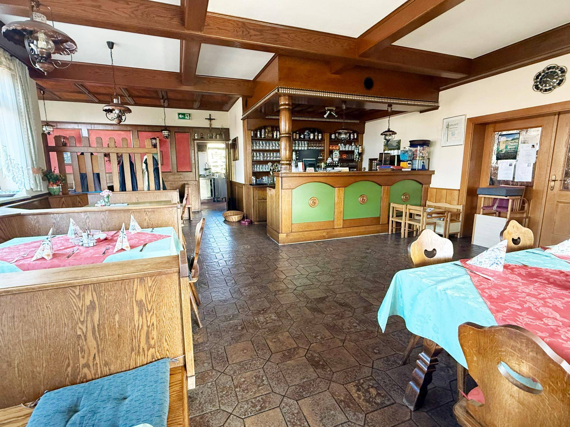 Rustikaler Gastraum mit Holzbalken, traditionellen Möbeln und einer Bar mit grünen Akzenten.