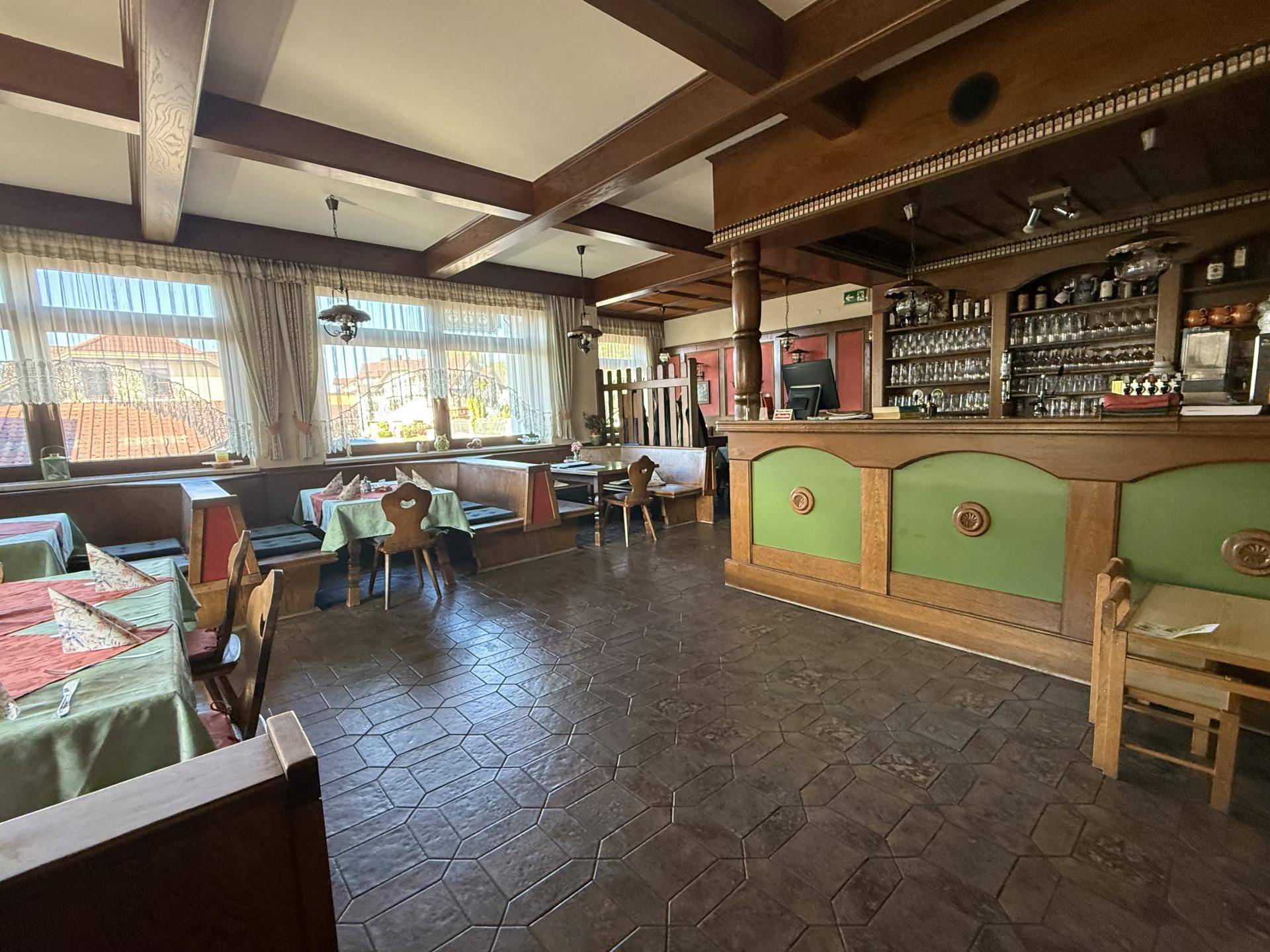 Geräumiger Gastraum mit Holzbalken, traditionellen Tischen und Bänken sowie einer gut ausgestatteten Bar.
