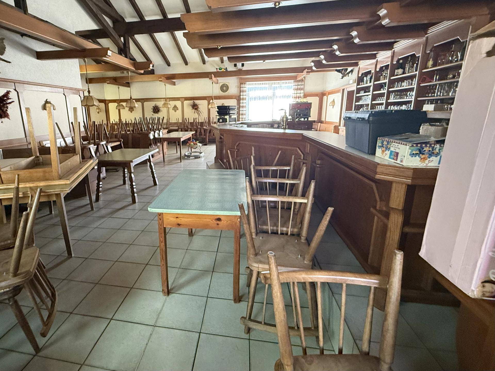 Geräumiger Gastraum mit Holzbalken, traditionellen Tischen und Bänken sowie einer gut ausgestatteten Bar.
