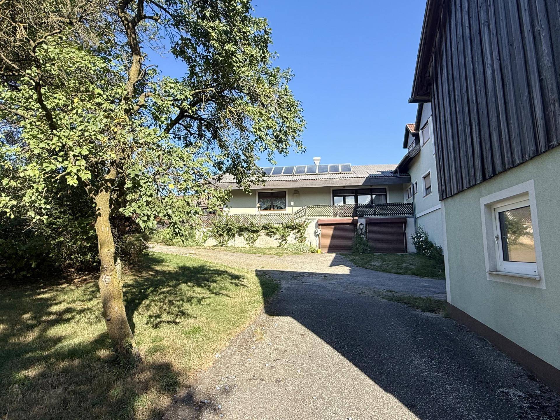 Gebäuderückseite mit Solarpaneelen auf dem Dach, umgeben von Bäumen und einem Schotterweg.