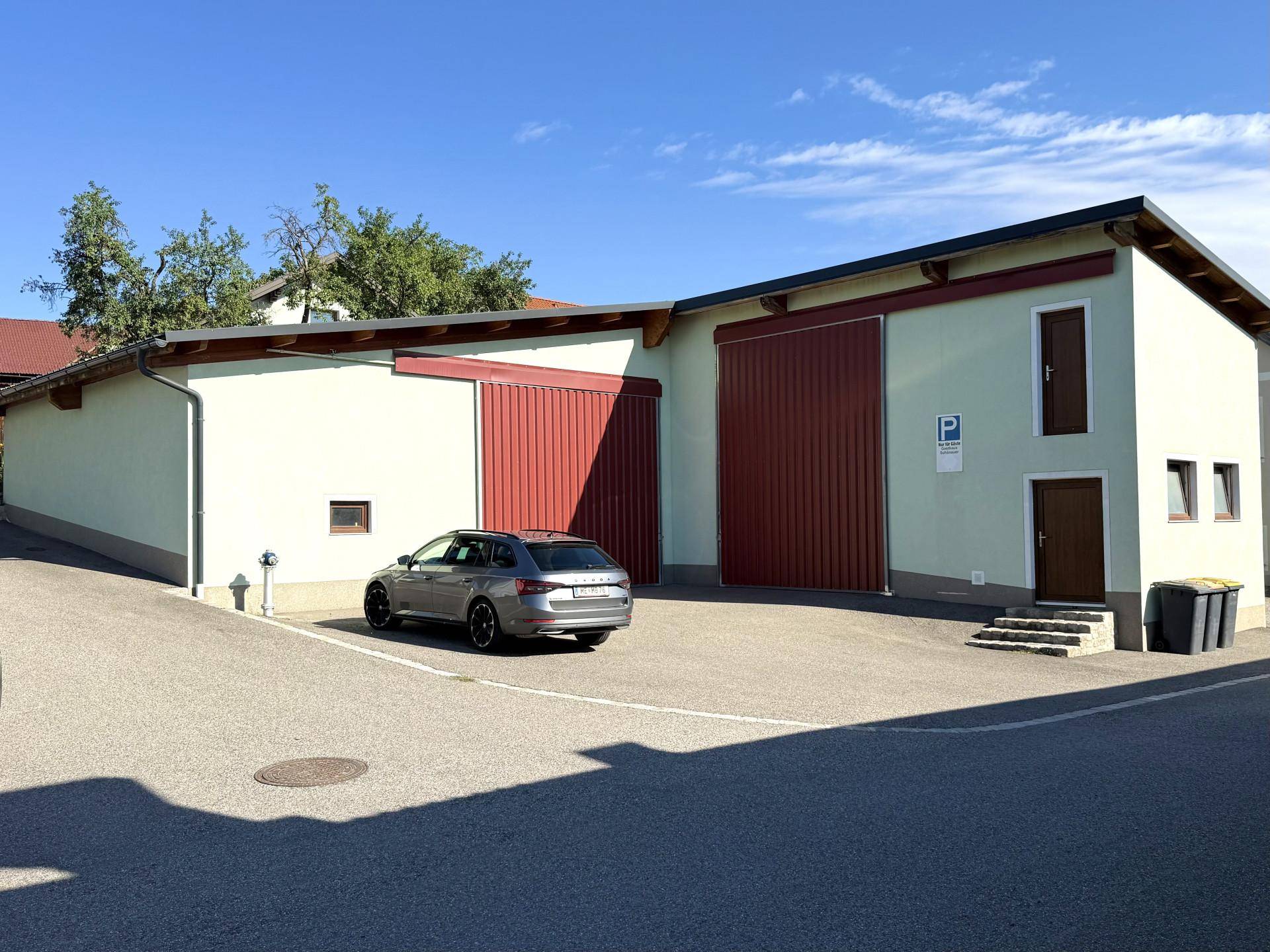 Modernisiertes Gebäude mit hellgrüner Fassade, roten Garagentoren und einem geparkten Auto.