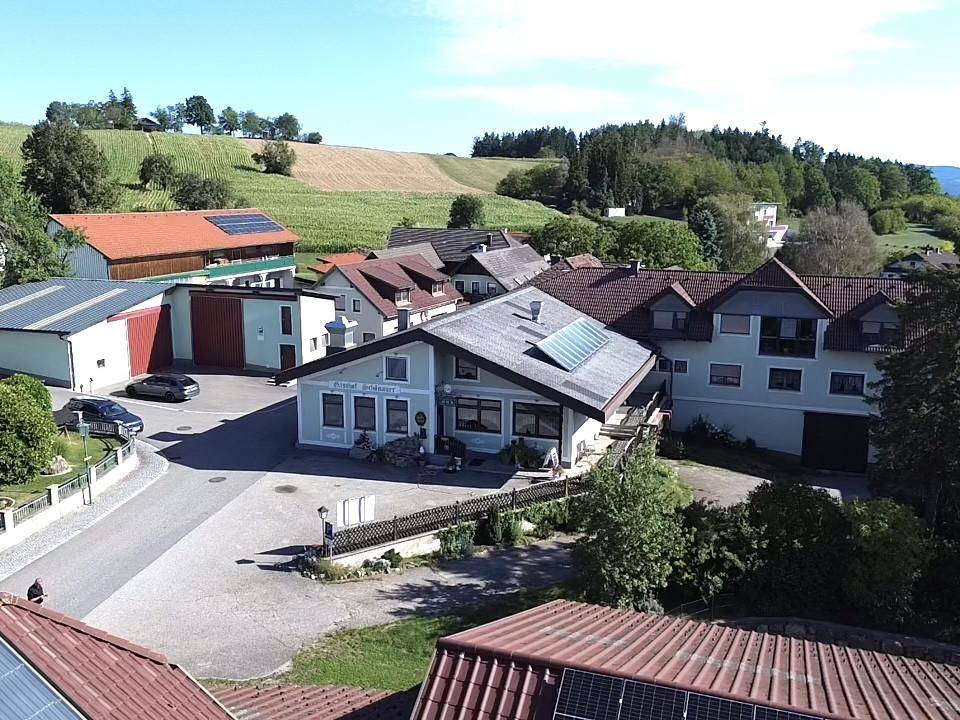 Luftaufnahme des Gasthofs Schönauer und der umliegenden ländlichen Bebauung mit Feldern im Hintergrund.