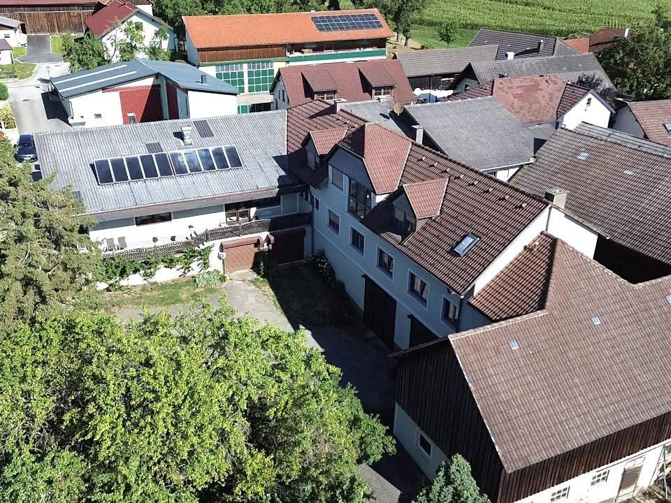 Luftaufnahme mehrerer Gebäude mit Dächern, die Solarpaneele und Gaubenfenster aufweisen, umgeben von Bäumen.