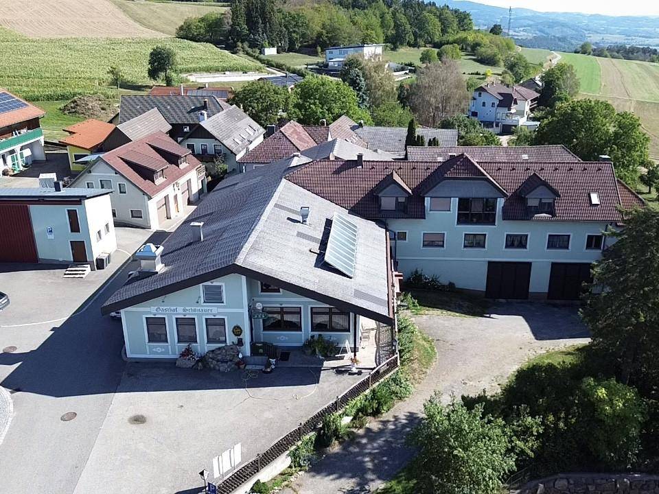 Luftaufnahme des Gasthofs Schönauer und angrenzender Gebäude, umgeben von Feldern und ländlicher Umgebung.