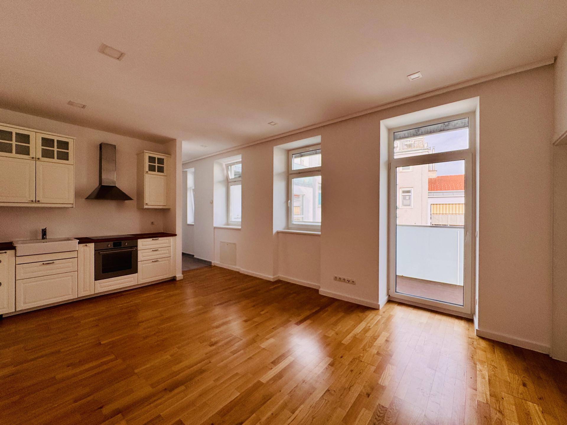 Heller offener Wohnbereich mit Holzboden, integrierter Küche und Zugang zu einem Balkon.