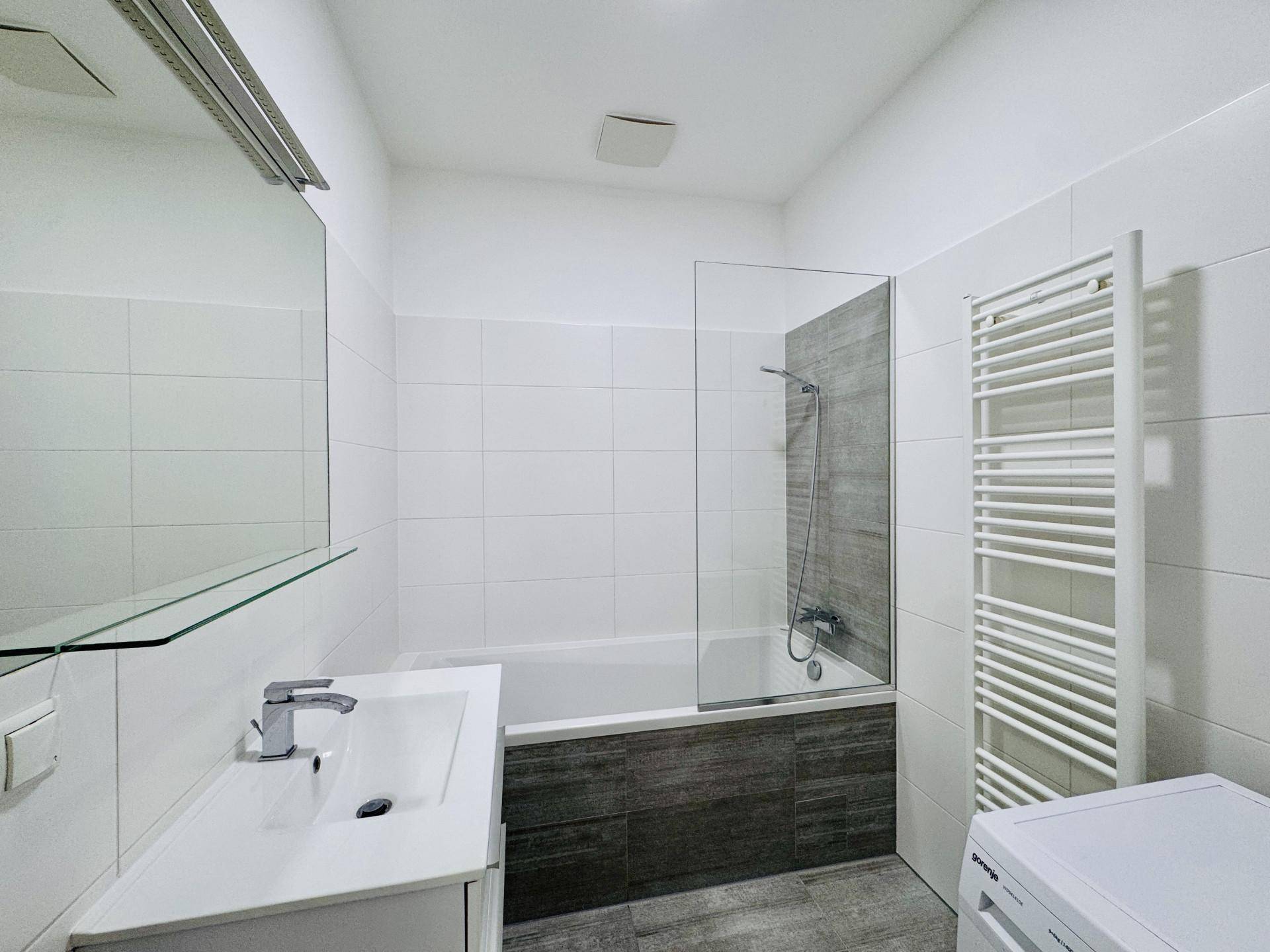 Modernes Badezimmer mit weißen Fliesen, Badewanne mit Duschwand, Einzelwaschbecken und Handtuchheizkörper.