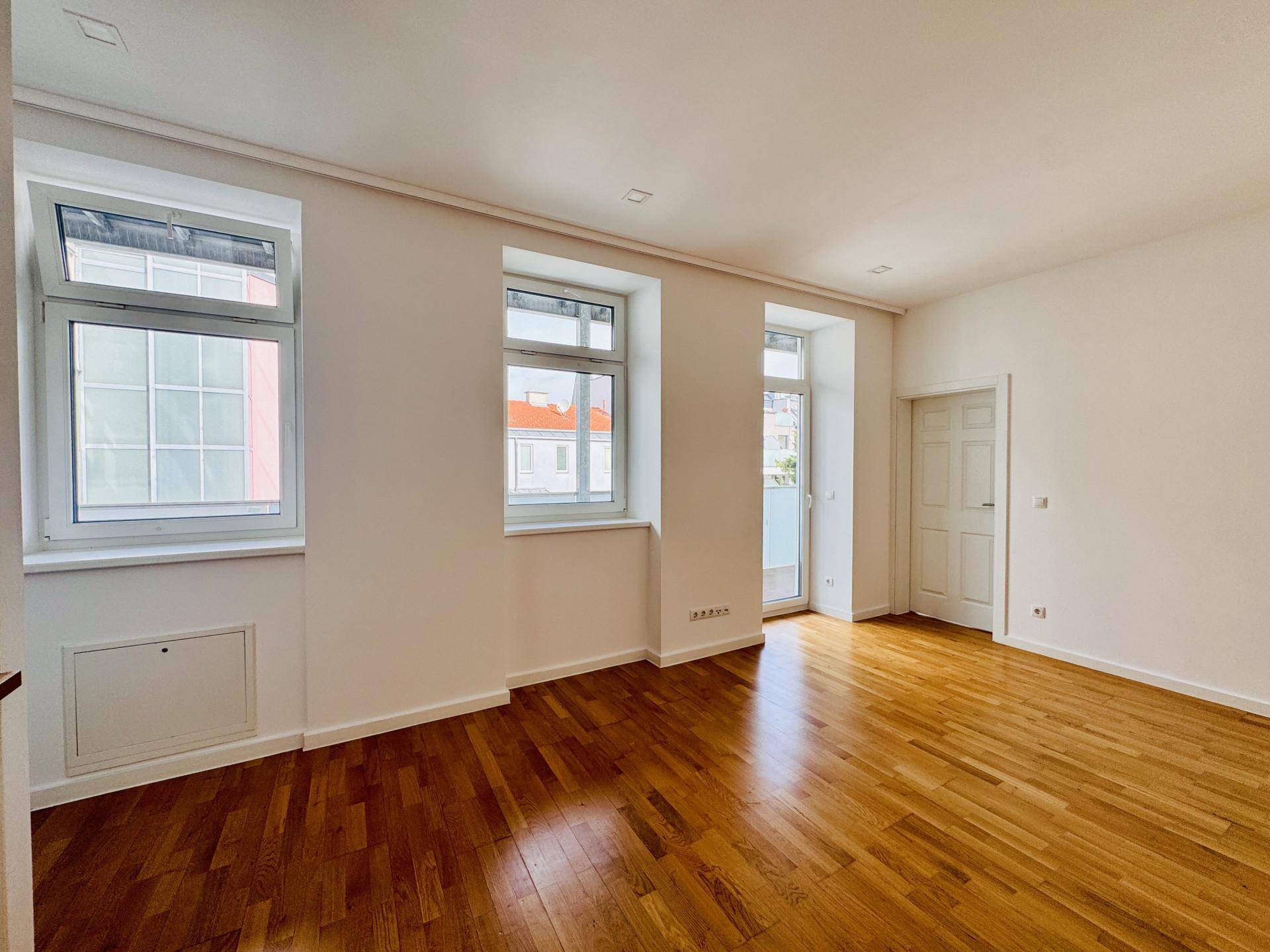 Heller Raum mit elegantem Holzboden, großen Fenstern und direktem Zugang zu einem Außenbereich.