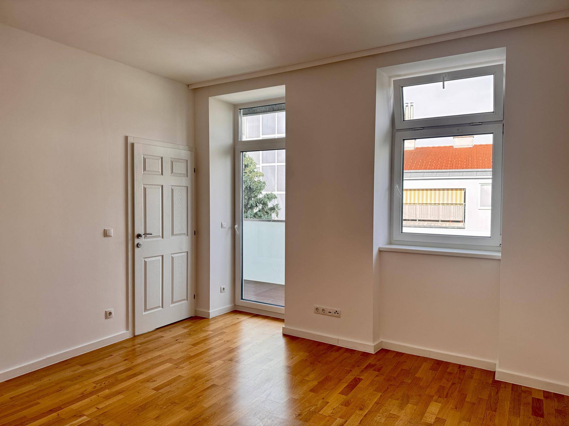 Helles Zimmer mit Holzboden, weiß gestrichenen Wänden und Zugang zu einem privaten Balkon.