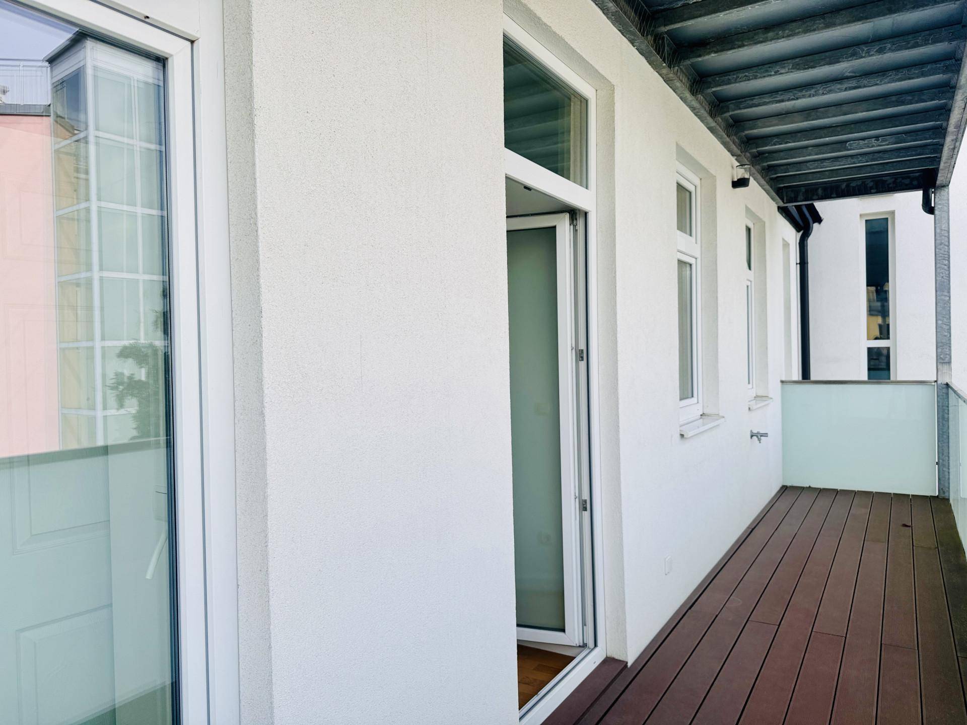 Langer Balkon mit Holzboden und Glasgeländer, der einen direkten Zugang zum Innenbereich bietet.