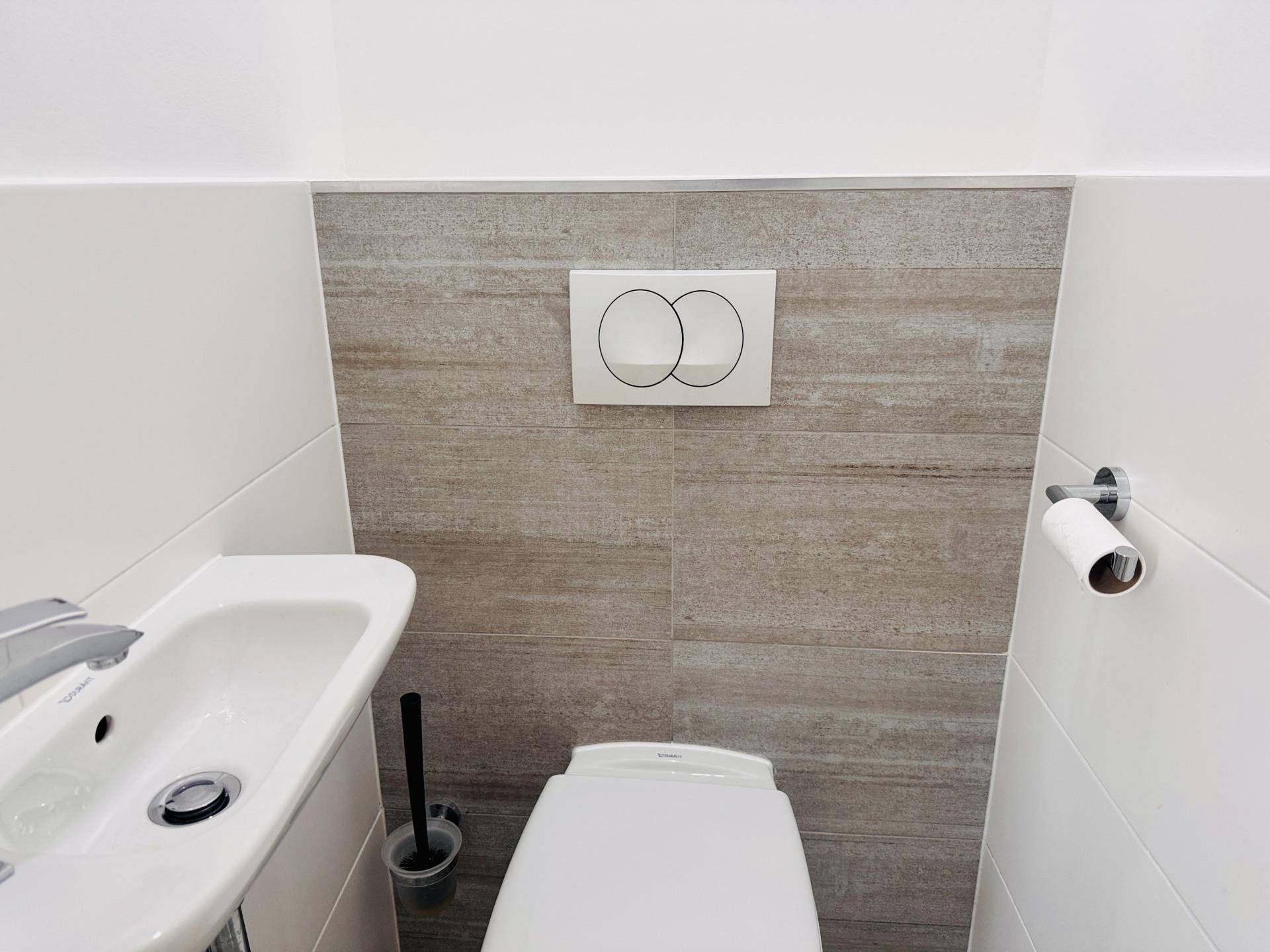 Modernes Gäste-WC mit wandhängender Toilette und kleinem Waschbecken, gefliesten Wänden.