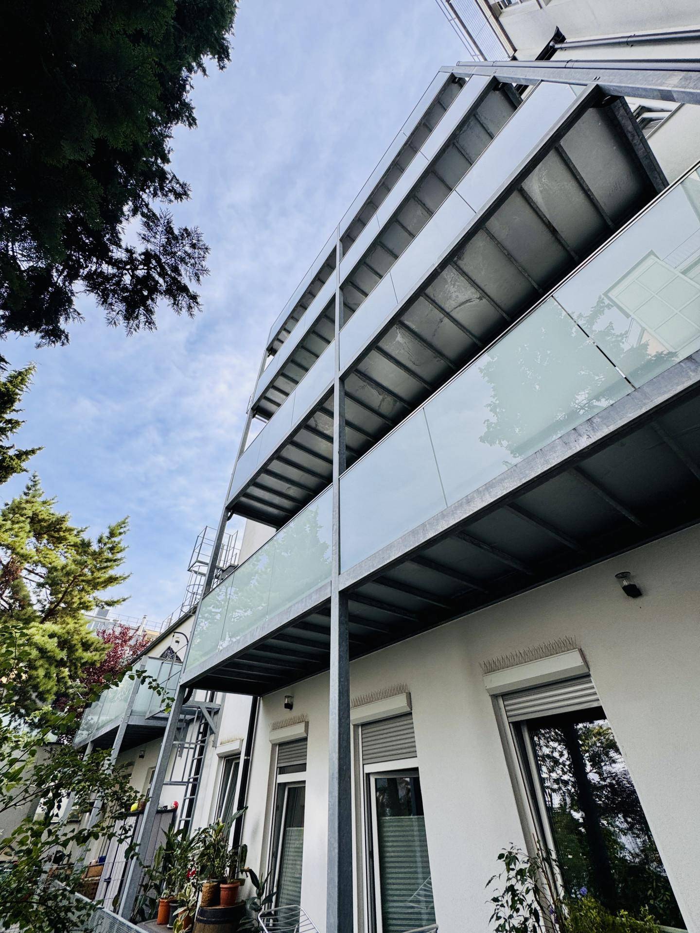 Moderne Gebäudefassade mit gestapelten Balkonen und Glasgeländern unter blauem Himmel.