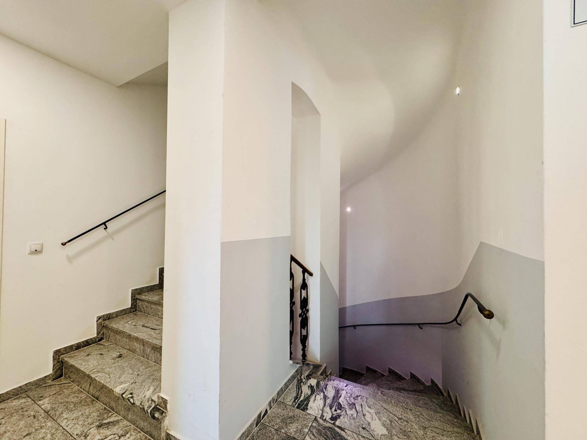 Treppenhaus mit Steinstufen und Geländer in einem gepflegten Mehrfamilienhaus.
