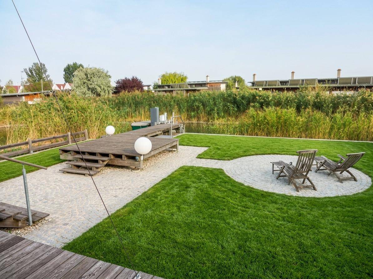 Gepflegter Gartenbereich mit Rasenfläche, gepflastertem Weg und Holzsteg am Wasser.