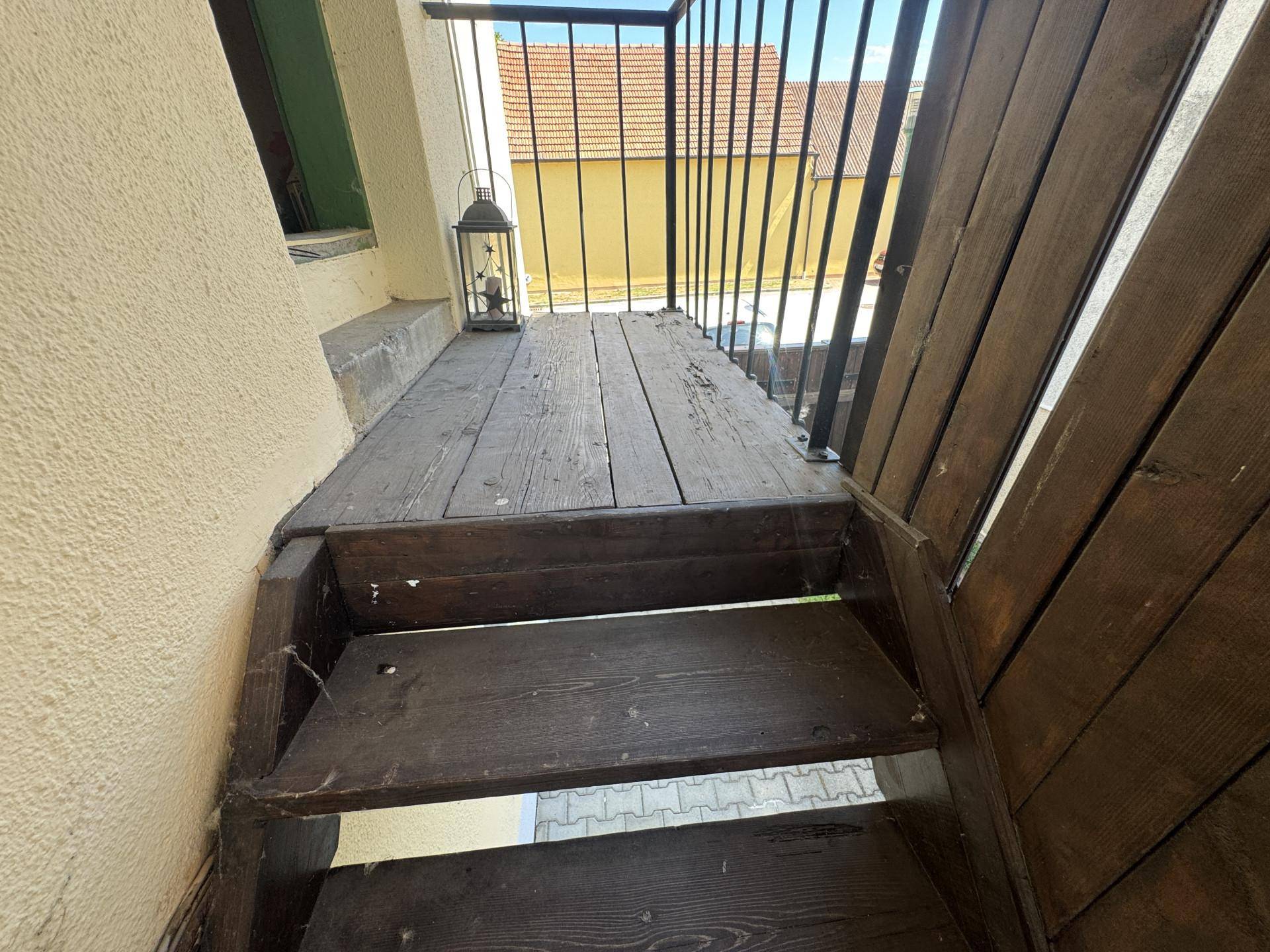 Rustikaler Holzbalkon mit Treppe und Metallgeländer, der einen Zugang zum Obergeschoss bietet.