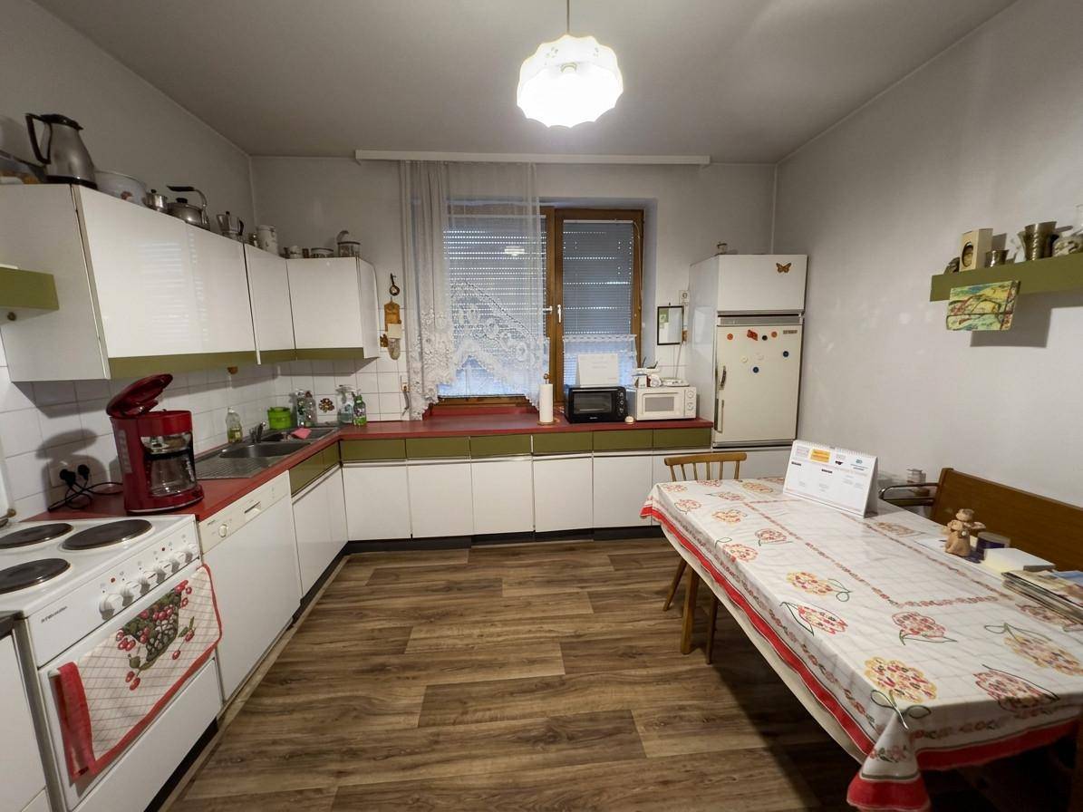 Funktionale Küche mit weißen Schränken, roter Arbeitsplatte und einem Essbereich am Fenster.