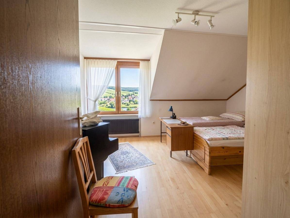 Schlafzimmer im Dachgeschoss mit zwei Betten, Schreibtisch und weitem Blick ins Grüne.