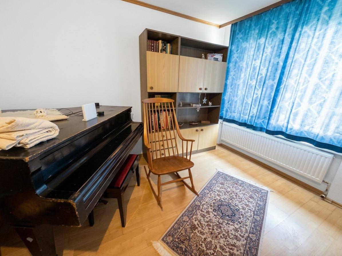 Helles Zimmer mit Klavier, Bücherregal und blauen Vorhängen, ideal als Arbeits- oder Musikzimmer.