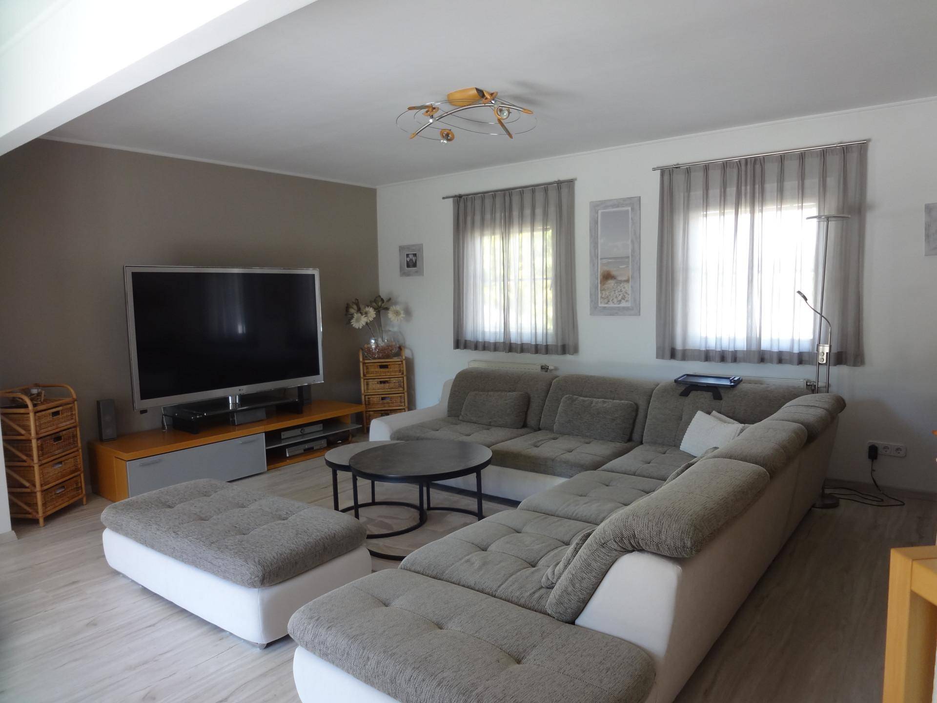 Gemütliches Wohnzimmer mit großem Ecksofa, Fernseher und hellem Laminatboden.