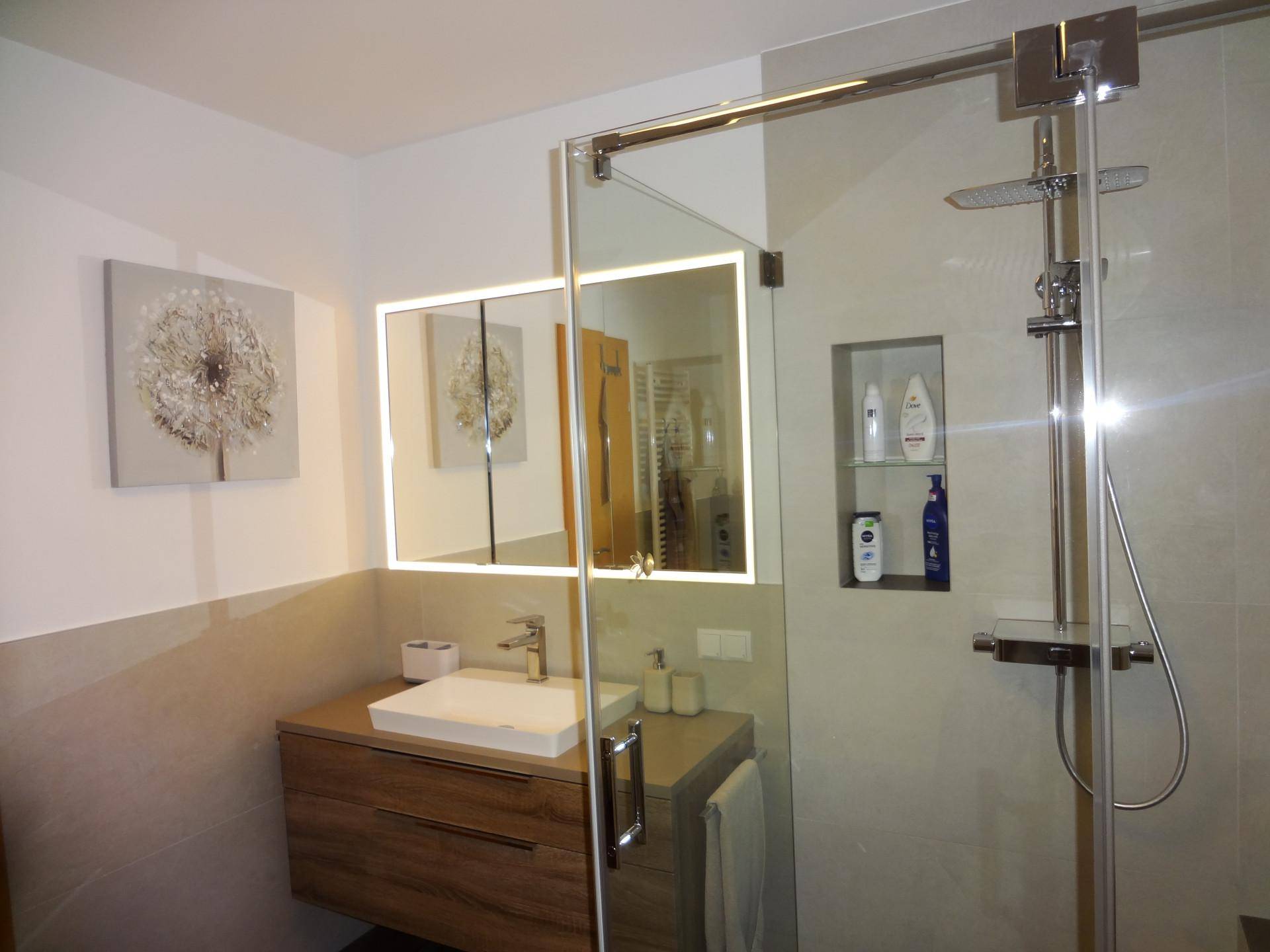 Modernes Badezimmer mit Waschtisch, beleuchtetem Spiegelschrank und begehbarer Dusche.