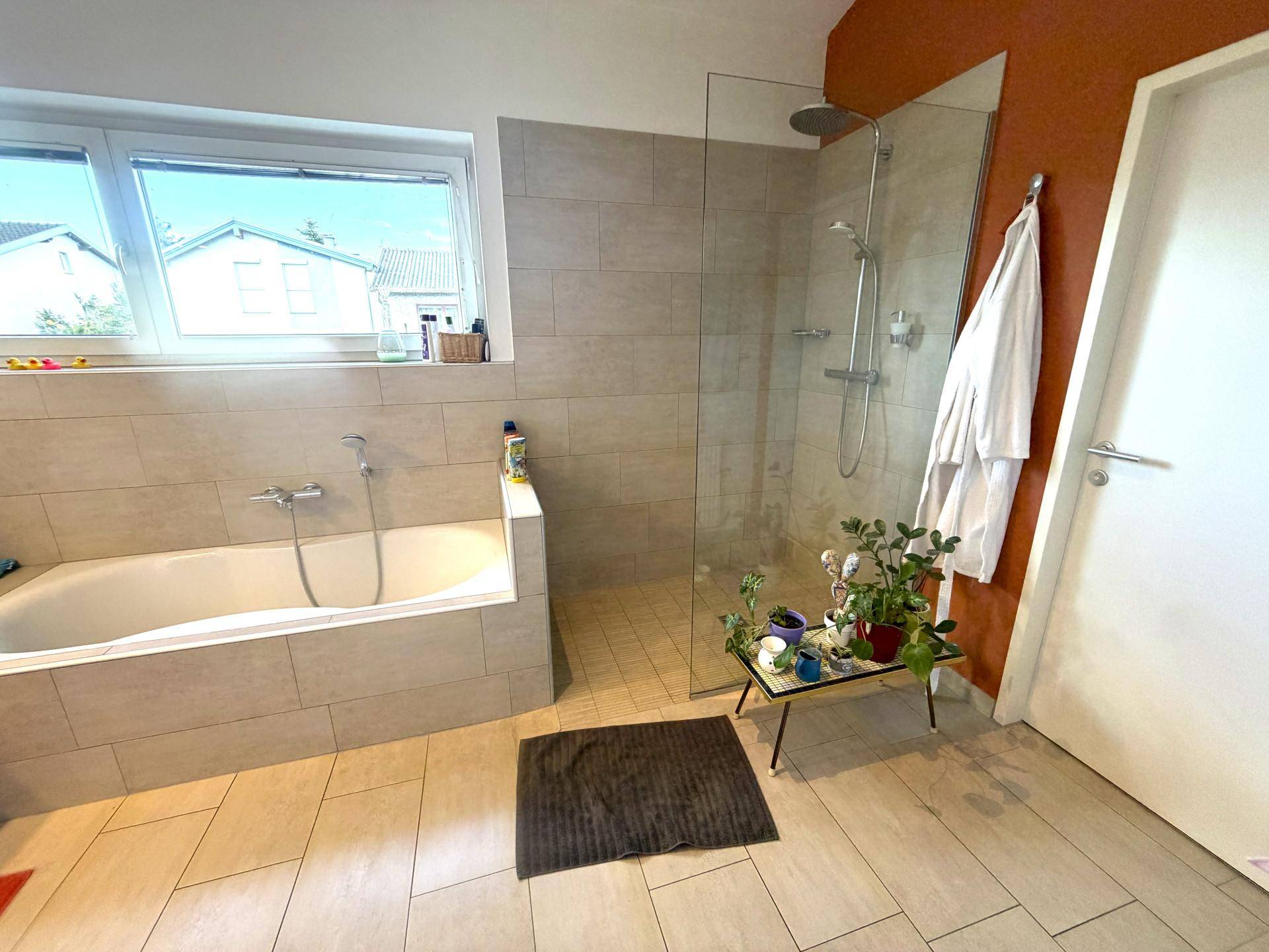 Geräumiges Badezimmer mit Badewanne, großer Dusche und Fenster für Tageslicht.