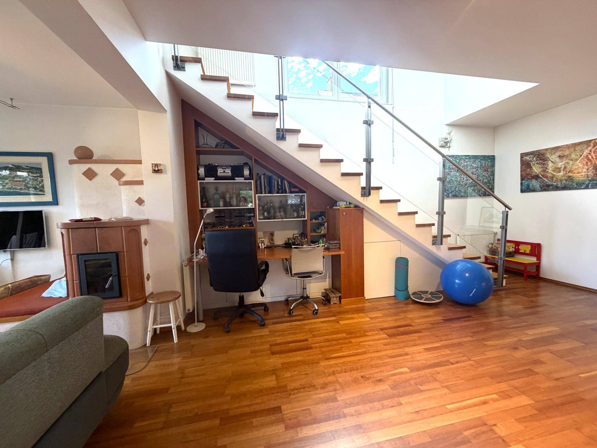 Wohnbereich mit traditionellem Kachelofen, Holzboden und integriertem Arbeitsplatz unter der Treppe.