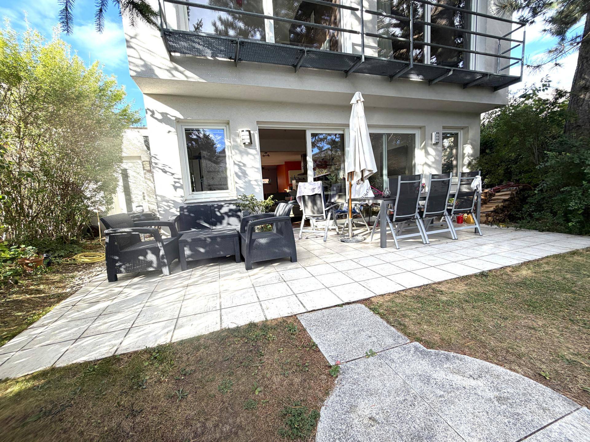 Große gepflasterte Terrasse mit Gartenmöbeln und Sonnenschirm im Außenbereich.