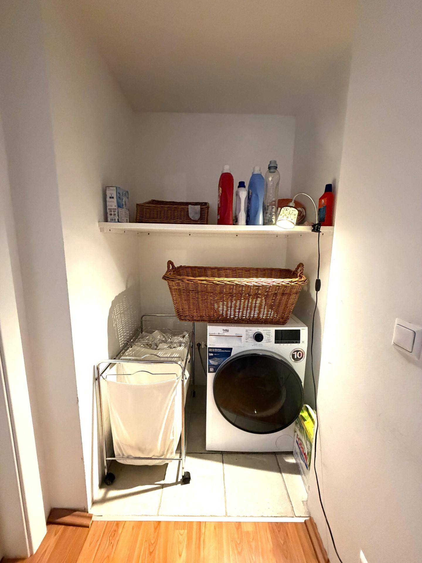Praktischer Hauswirtschaftsraum mit Waschmaschine, Regalen und Fliesenboden für effiziente Organisation.