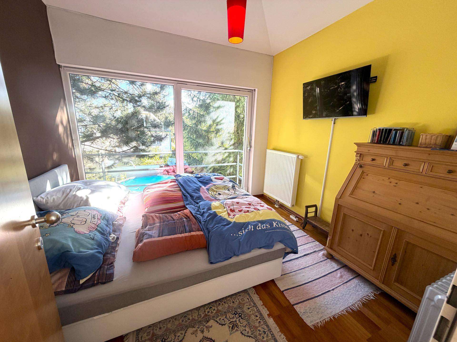 Helles Schlafzimmer mit Doppelbett, Holzboden und Zugang zum Balkon.