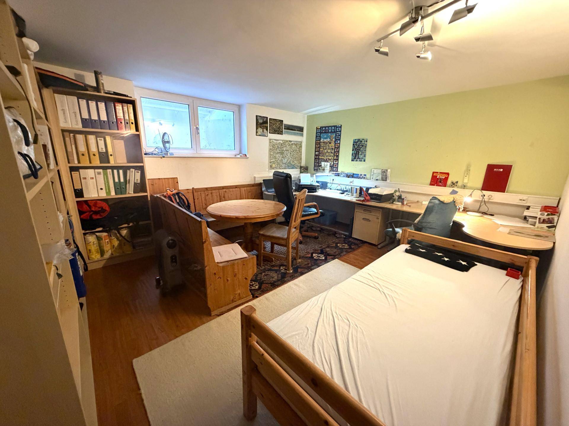 Geräumiges Arbeitszimmer im Untergeschoss mit Schreibtischen, Regalen und Sitzbank.