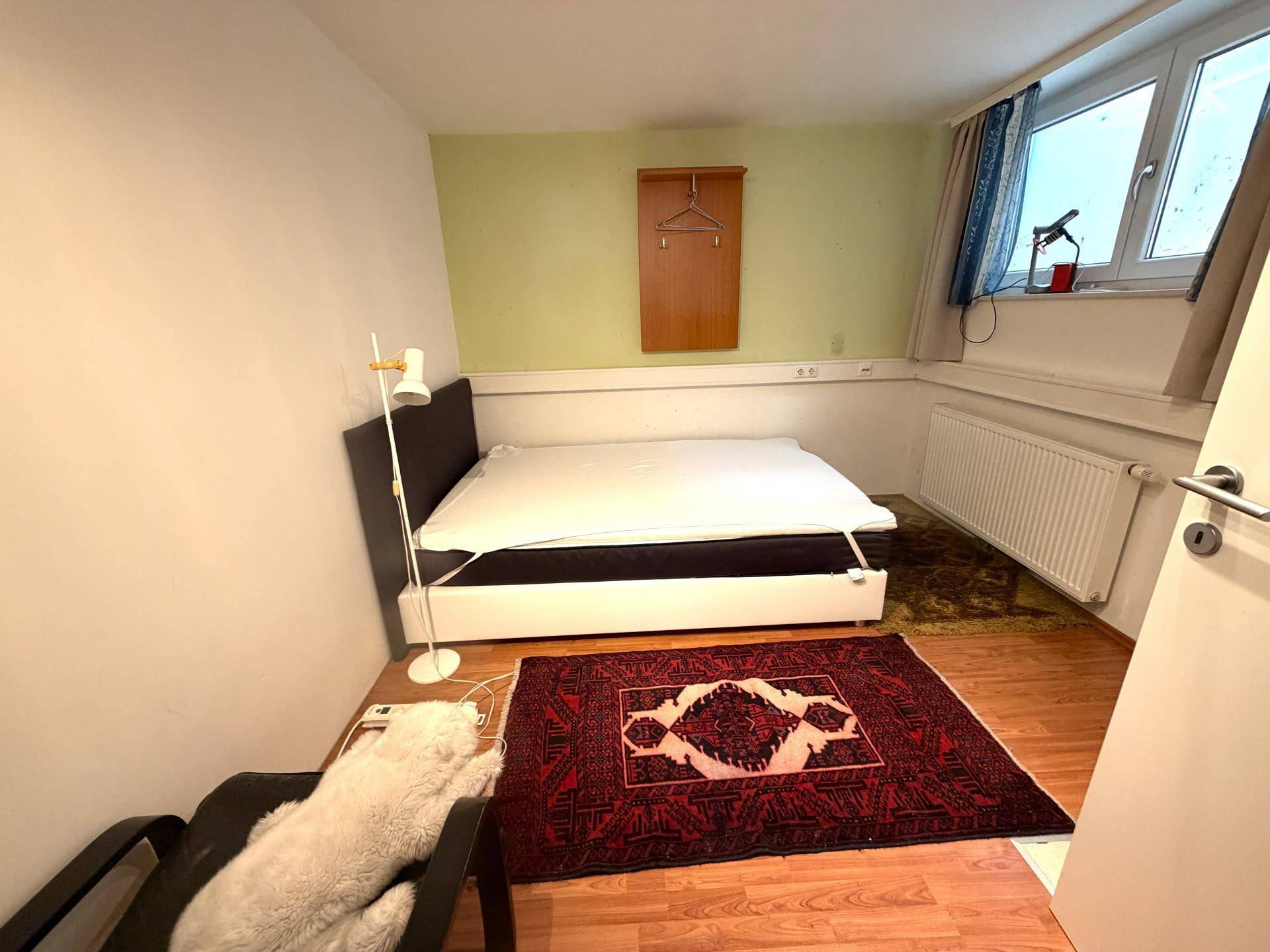 Schlafzimmer mit Holzboden, einem Bett und einem traditionellen Teppich, hell und funktional.