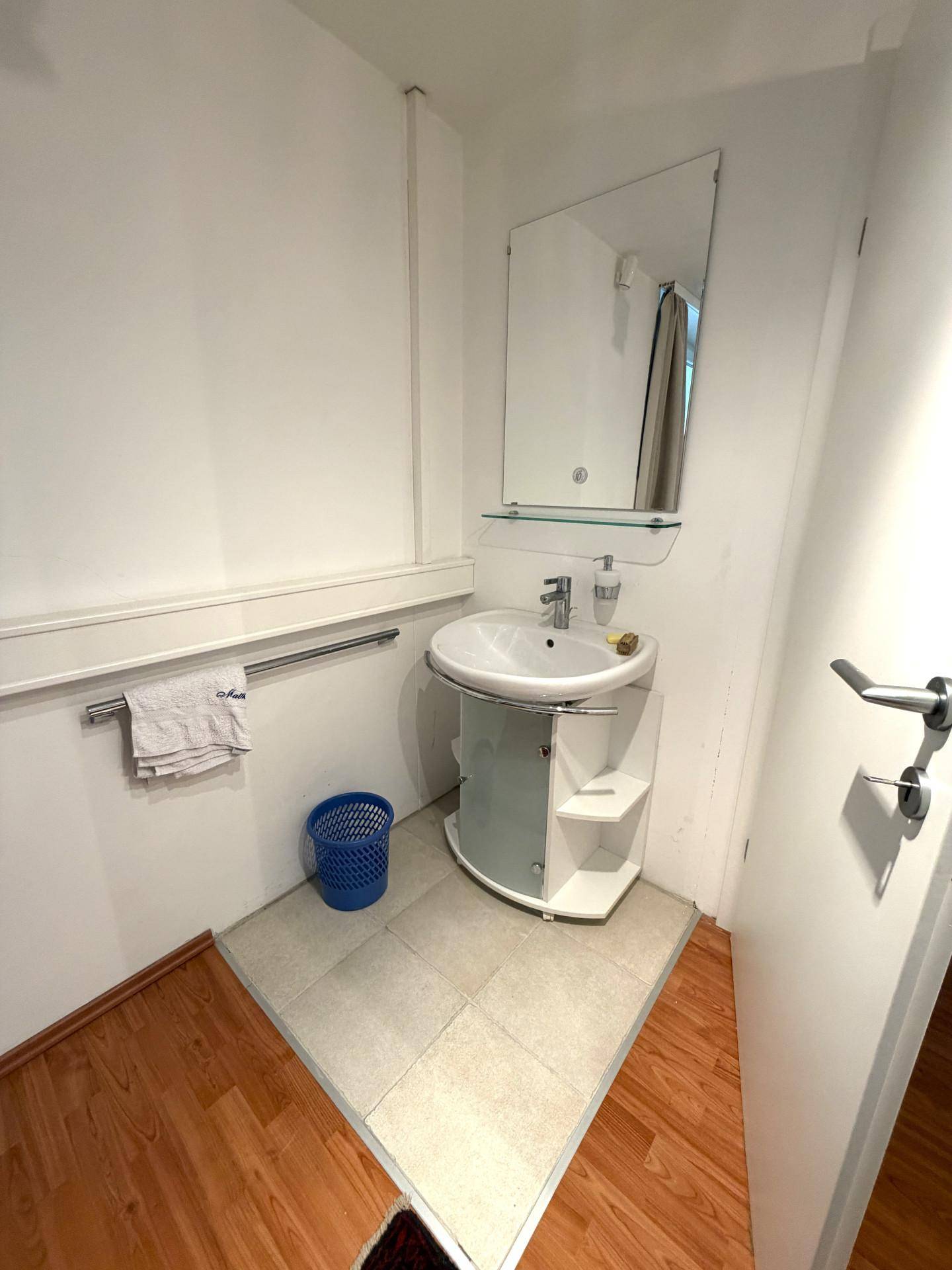 Kleines Badezimmer mit modernem Waschbecken, Spiegel und Holzboden, ideal als Gästetoilette.