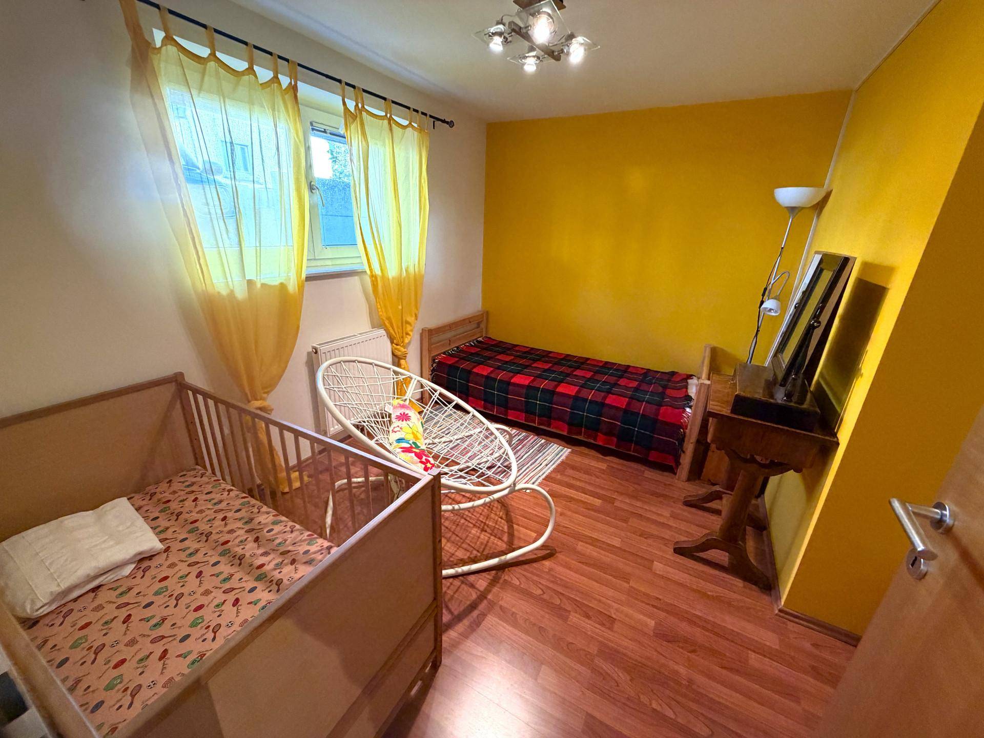 Helles Schlafzimmer mit zwei Betten, Holzboden und einer auffälligen gelben Wand für eine lebendige Atmosphäre.