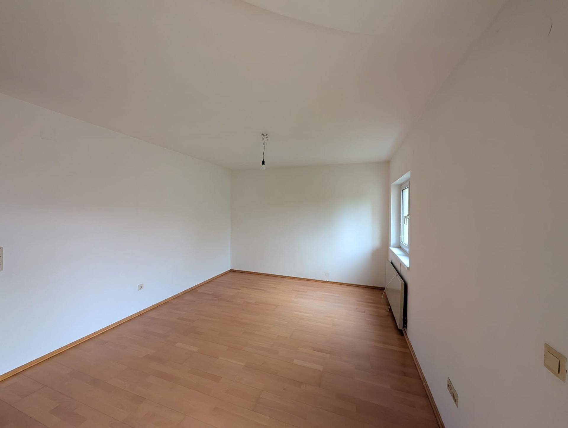 Helles, leeres Zimmer mit Parkettboden und Heizkörper unter dem Fenster.
